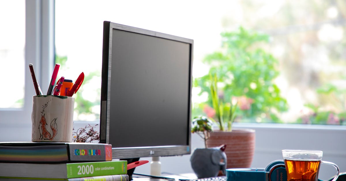 Modern office desk setup with a computer, books, and a cup of tea for a creative work environment.