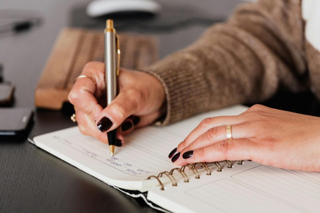 pexels-photo-4476376-4476376 Crop unrecognizable female with stylish manicure sitting at black desk with keyboard and smartphone and taking notes with silver pen in notepad