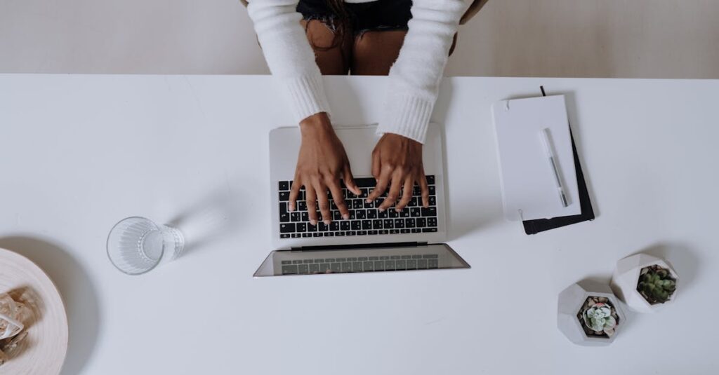 Top view of a woman typing on a laptop at a modern, minimalist home office desk with plants.