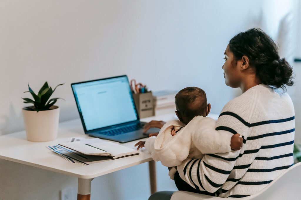 pexels-photo-6393356-6393356 Pensive ethnic woman in casual clothes slitting with baby while browsing netbook in light room in apartment in daytime