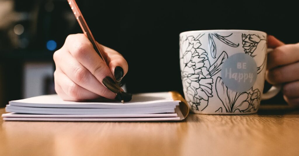 pexels-photo-851213-851213 Person writing in a notebook with a floral ceramic mug on a wooden desk.